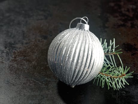 Silver bauble Christmas decoration with a ridged pattern with a twig of pine needles on a dark background with copyspace for your seasonal message