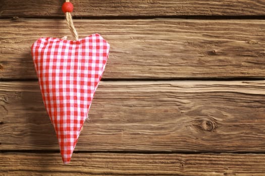 Handmade rustic hanging red and white checked heart ornament for Christmas or Valentines Day for a sweetheart or loved one with copyspace on a wooden background