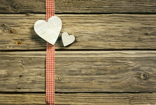 Romantic Christmas background with hearts on a red and white checkered country ribbon lying on textured rustic wooden boards with copyspace