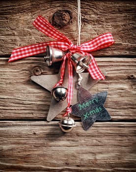 Traditional Christmas decoration with checkered bow, silver bells and star shapes wishing Merry X-mas, hanging on a rustic wooden wall