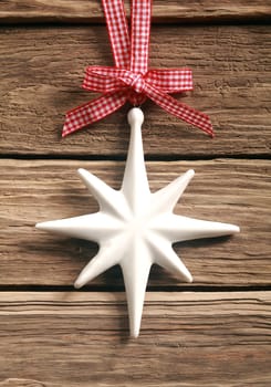 Decorative white Christmas star hanging from a rustic red and white checkered bow and ribbon on a textured weathered wooden boards background