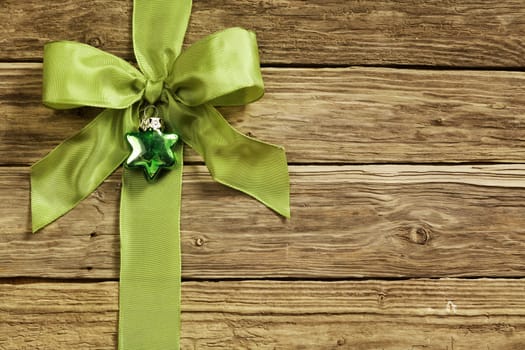 Stylish green ribbon and heart decoration tied in an ornamental bow on textured rustic wooden boards for your Xmas greeting or seasonal message