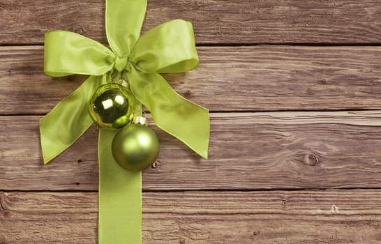 Decorative green bow decorated with two Christmas bauble ornaments on a wooden background with copyspace for your seasonal greeting
