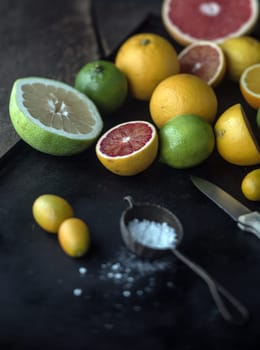 Preparing assorted citrus fruit for dessert with whole and halved grapefruit, oranges, limes, lemon and kumquat on a rustic kitchen counter with powdered sugar and a knife