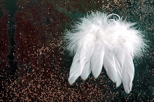 Soft white Christmas angel wings made from birds feathers on a dark background with glitter for a seasonal Xmas background with copyspace for your greeting or invitation