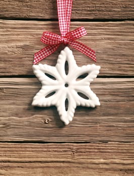 Rustic Christmas background with a white wintry snowflake decoration hanging on a red and white ribbon tied in an ornamental bow, on wooden boards with copyspace