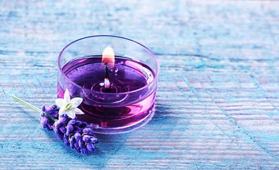Aromatherapy spa background with a sprig of fragrant lavender alongside a burning candle with essential oil and plant extracts in a wellness and spirituality concept with copyspace