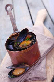 Serving of delicious gourmet freshly steamed marine mussels in a copper pot with an open one displayed below on a napkin in a rustic kitchen