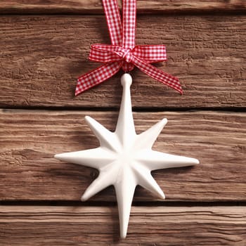 White Christmas star ornament hanging from a pretty red and white checked ribbon and bow on rustic textured wood in square format