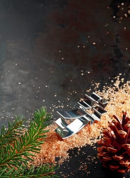 Christmas baking still life with a star shaped cookie cutter and caramelized sugar on a dark background with a decorative pine cone and fresh green pine branch, with copyspace in vertical format