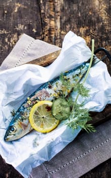 Preparing an baked fish in foil with sliced lemon, spices and assorted fresh herbs for cooking on an open barbecue fire or in the oven, high angle view in a rustic kitchen
