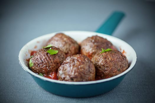 Serving of tasty spicy meatballs seasoned with fresh herbs and a tomato based sauce, close up view with shallow dof in a blue saucepan