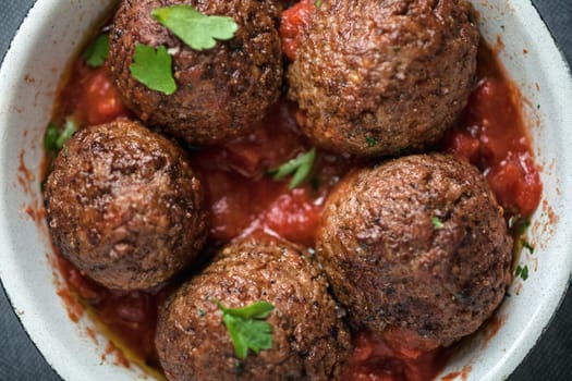 Serving of delicious seasoned meatballs in tomato sauce garnished with fresh herbs, overhead view in a saucepan
