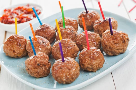 Buffet display of tasty spicy meatballs with colorful toothpicks for dipping arranged on a plate