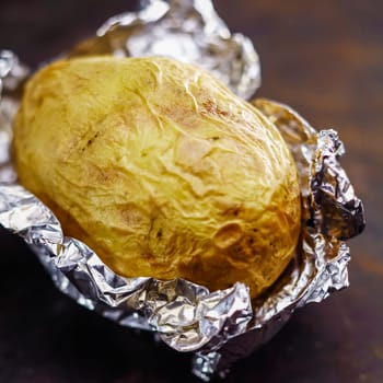 Delicious hot baked potato in aluminium foil fresh off the summer barbecue still lying on its silver wrapping