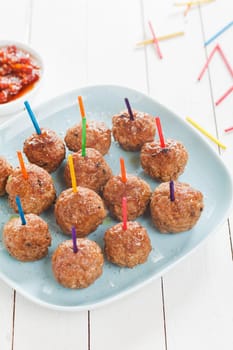 Preparing a tray of delicious spicy seasoned meatballs with colored toothpicks for snacks at a catered event , high angle view on a plate on rustic white boards