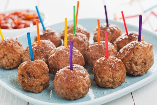 Tray of savory spicy meatballs for appetizers arranged on a tray on a buffet with colorful toothpicks to enable them to be dipped in sauce