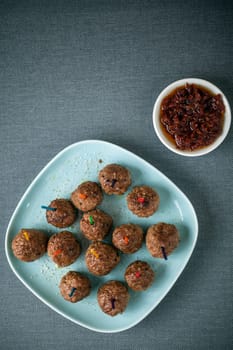 Overhead view of a plateful of seasoned meatballs and savory spicy tomato and chili pepper dip for appetizers, overhead view on a grey tablecloth with copyspace