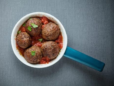 Tasty seasoned meatballs in a saucepan with a hot spicy chili pepper and tomato sauce and fresh herbs, overhead view