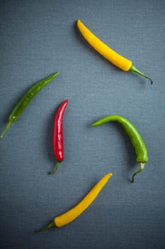 Colorful assorted red, green and yellow fresh chili peppers for use in cookinng as a hot pungent spice lying on a textured grey cloth, overhead view with copyspace
