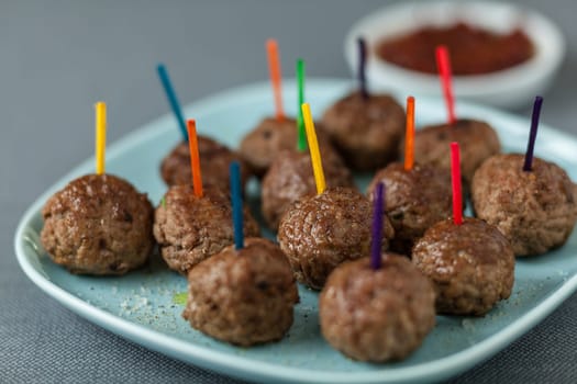 Plate of seasoned beef meatballs for appetizers with colorful toothpicks and a tangy savory dip