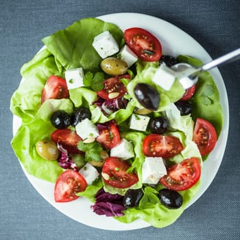 Plate of healthy Mediterranean salad with feta cheese, black and green olives, tomato and lettuce , close up overhead view in square format