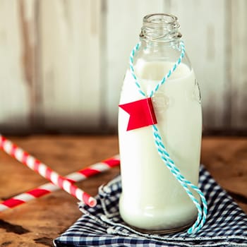 Glass bottle of fresh full cream farm milk with a label attached on a string served with two straws on a rustic checkered blue and white napkin