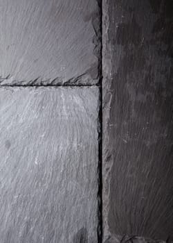 Textured background pattern of natural dark grey slate tiles abutting each other with rough surfaces and slightly chipped edges