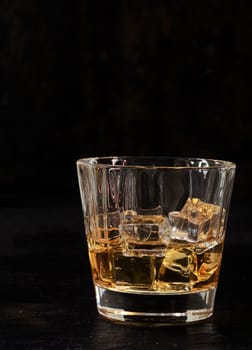 Iced bourbon or whiskey in a glass tumbler on a dark background with vertical copyspace