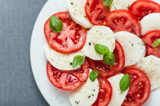 Colorful red and white Italian Caprese salad viewed from above with alternating slices of ripe red tomato and mozzarella cheese seasoned with fresh basil