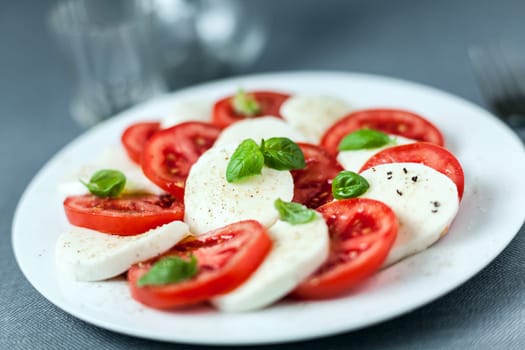 Healthy Italian Caprese salad served on a plate with alternating slices of white mozzarella cheese and ripe red tomato topped with fresh basil