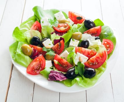 Fresh Mediterranean salad with feta cheese, olives, lettuce, fresh herbs and tomato drizzled with olive oil for a healthy diet, high angle on white boards