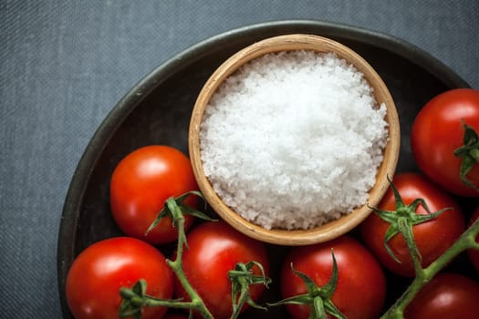 View from above of a bowl of coarse natural sea or rock salt for cooking with fresh ripe red cherry tomatoes on a plate ready for use in the kitchen