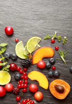 Colorful healthy sliced fresh fruit , assorted berries and herbs on a textured dark grey slate background with copyspace, view from above