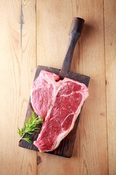 Raw t-bone or porterhouse steak with a sprig of fresh rosemary on a vintage wooden board , overhead view on wood with copyspace