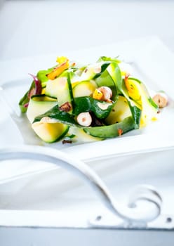 Delicious healthy fresh summer salad served outdoors on a white table in sunlight with the scrolled white metal arm of garden furniture in the foreground