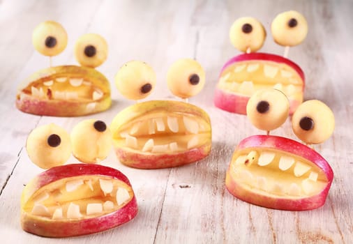 Spooky Halloween party favors or decorations made from fresh apples and dough in the form of open mouths lined with teeth topped with round googly eyes on a rustic table, creative country handicraft