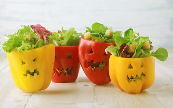 Colorful Halloween food background with colorful healthy stuffed red and yellow sweet bell peppers with cutout faces in the skin like Halloween jack-o-lanterns filled with green salad and cheese