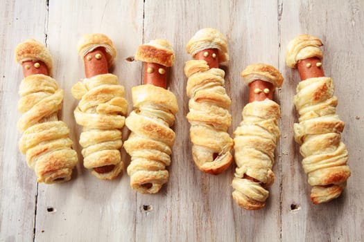 Six Weiners Wrapped in Pastry to Look Like Halloween Mummies on Wooden Background