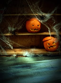 Two Halloween Jack o Lanterns Carved from Oranges and Spiderwebs with Spiders on Shelves Blurred in Background with Foreground Space