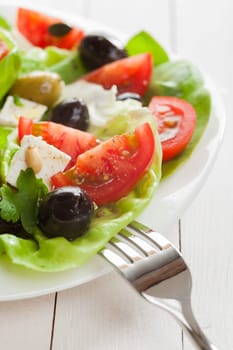 Fresh healthy vegetarian diet with a plate of delicious Mediterranean salad with tomato, olives, feta cheese , lettuce and herbs, partial view on white boards