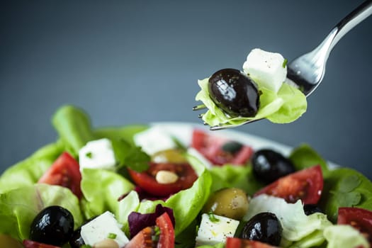 Enjoying a healthy Greek salad of feta cheese, olives tomatoes and leafy green with a fork suspended above the plate with lettuce, feta and olive on it
