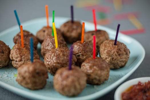 Plate of tasty spicy savoury meatballs for party snacks with colorful toothpicks for dipping in a bowl of piquant sauce