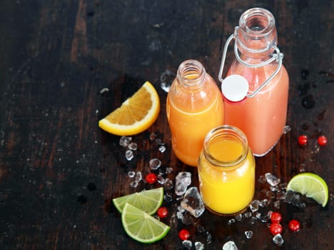 Preparing tasty healthy summer fruit juices in glass bottles with slices of fresh orange, lemon, lime and cranberries, viewed high angle on a dark rustic wooden surface with copyspace