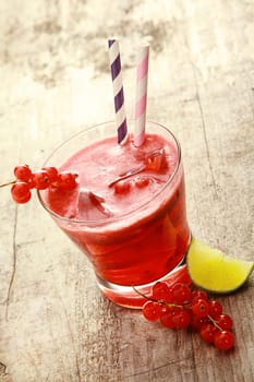 Tumbler of delicious refreshing redcurrant juice with fresh berries and a lemon wedge on a rustic wooden table outdoors in summer sunlight