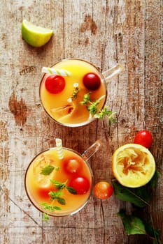 Glasses of fresh summer fruit cocktail with blended fruit juices garnished with fresh cranberries and herbs on a rustic wooden table, overhead view