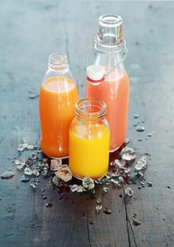 Healthy fresh home made fruit juices in glass bottles and jars chilled with ice standing on a dark table outdoors in the garden for tasty organic summer refreshments