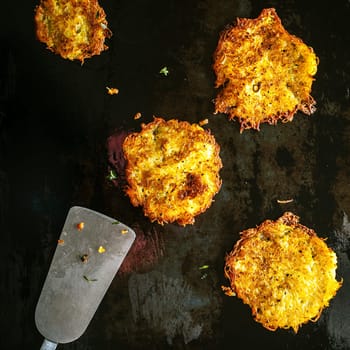 Golden German potato fritters made from grated seasoned fresh potatoes frying on a griddle with an old metal spatula, viewed from above