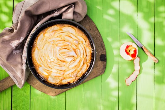 Delicious golden home baked apple pie viewed from above in an oven dish on a green wooden garden table in dappled sunlight for a relaxing summer meal and dessert