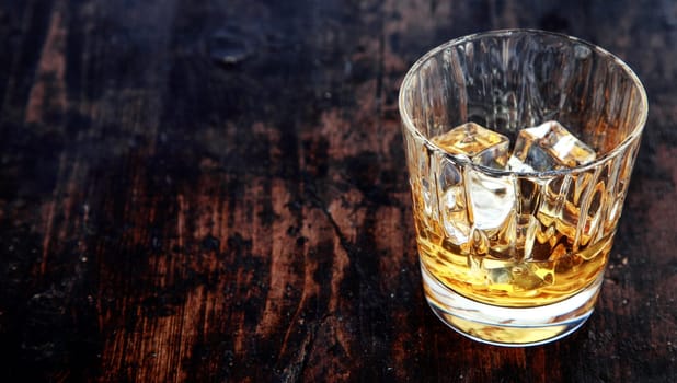 Close-up of a glass of whiskey, bourbon or scotch, with ice cubes, on an old rustic wooden table